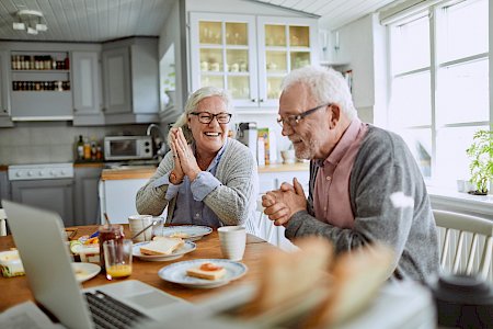 Glückliches älteres Ehepaar reibt sich beim Frühstück nach Rentenabrechnung die Hände